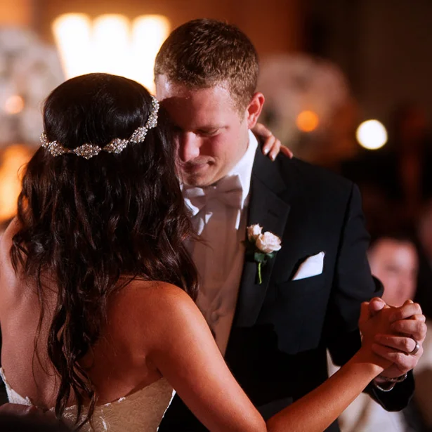 Bride and groom sharing a close moment during their first dance, heads touching gently in soft evening light.
