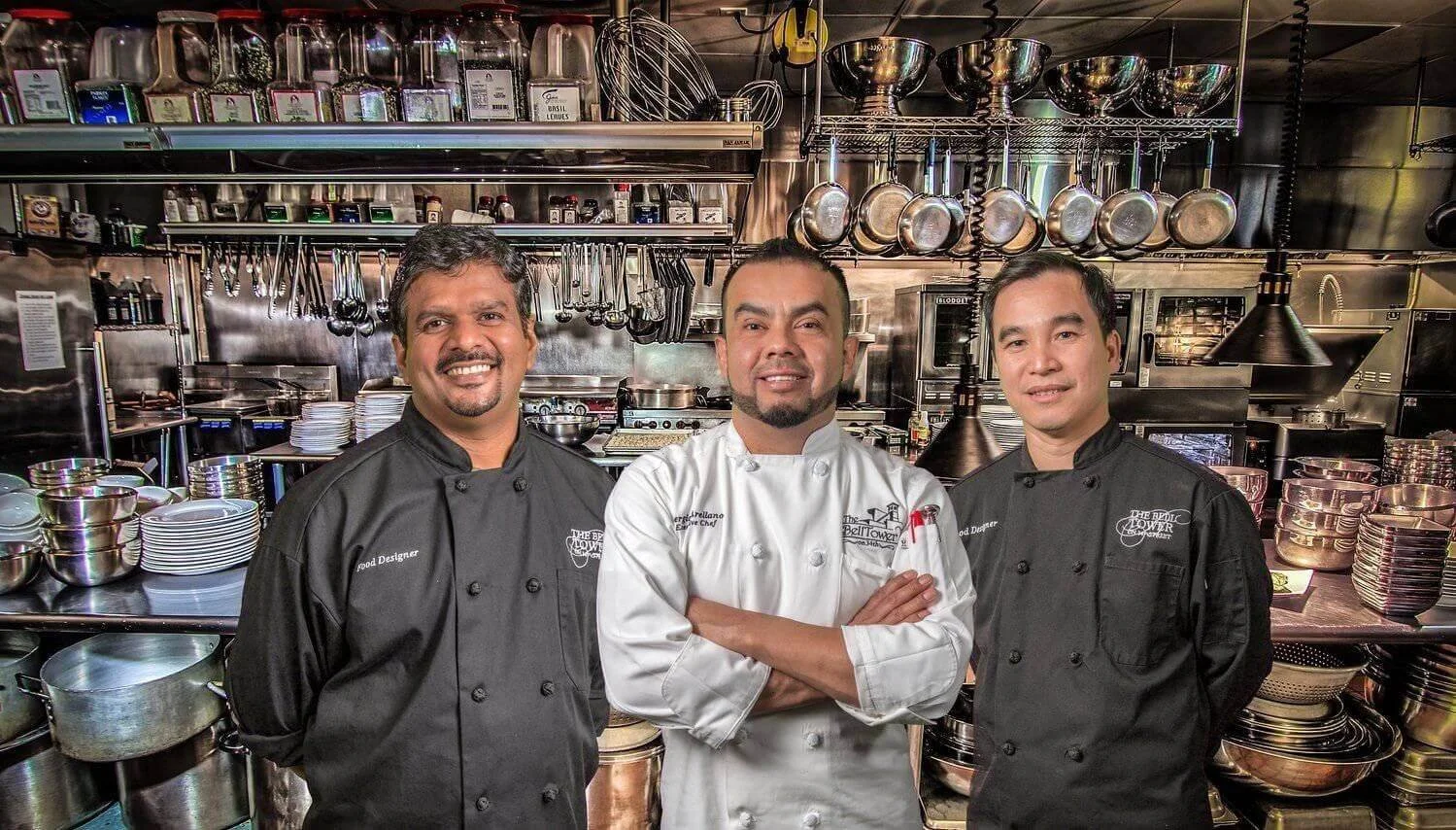Three smiling professional chefs in a state-of-the-art commercial kitchen, highlighting the exceptional in-house catering service.